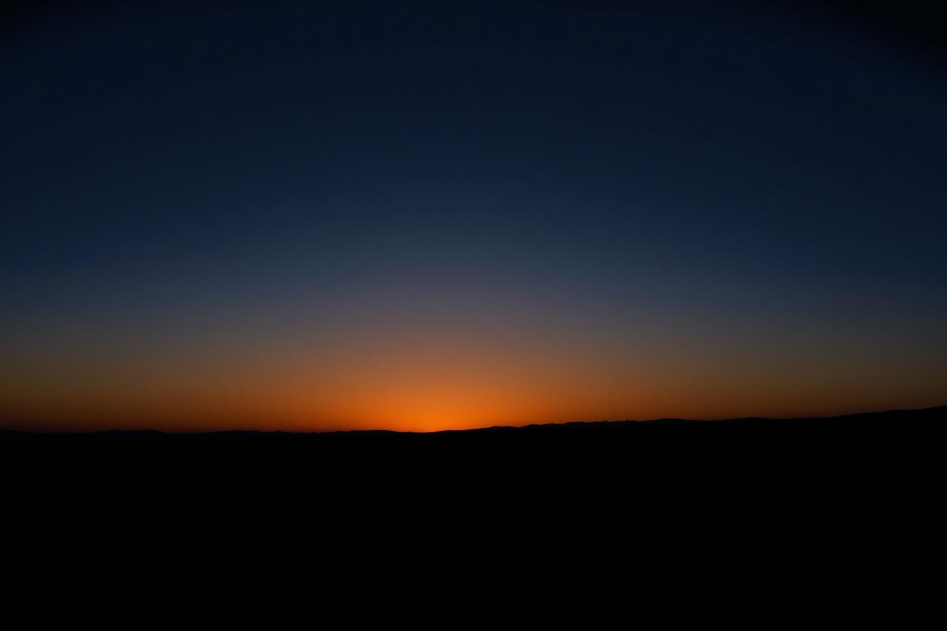 First light of dawn — warm gold at the horizon under a deep blue sky