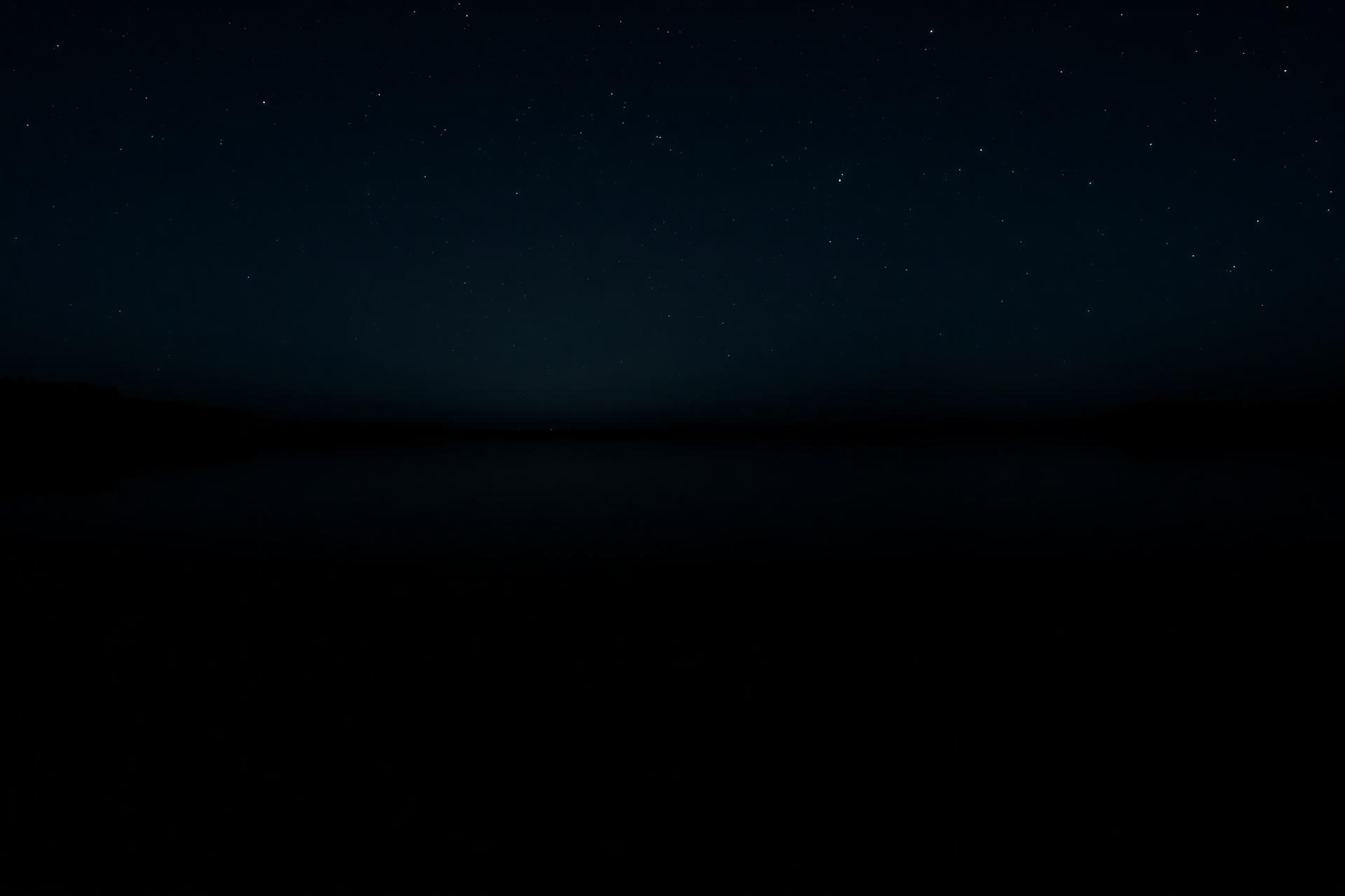A still black lake at night reflecting the starry sky